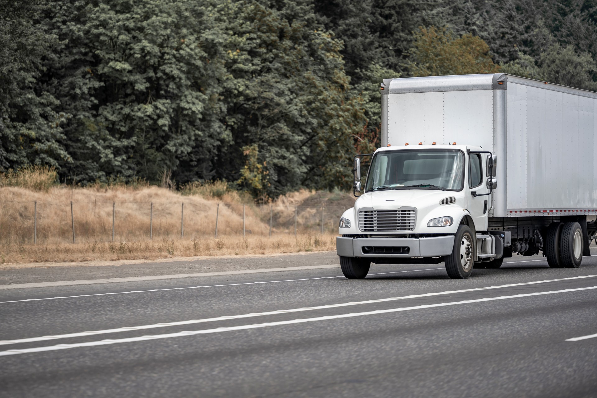 Small compact rig white semi truck with long box trailer moving on the highway road for local cargo delivery